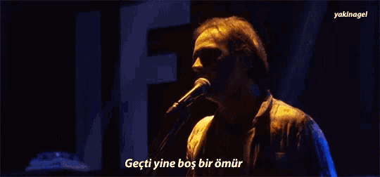 a man playing a guitar and singing into a microphone with the words " geçti yine bas bir omur " below him