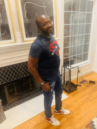a man wearing a superman t-shirt stands in front of a fireplace