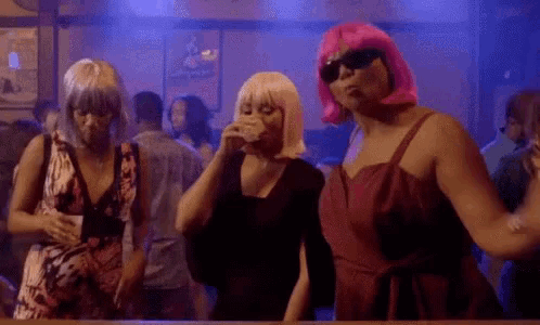 three women in pink wigs are dancing in a club .
