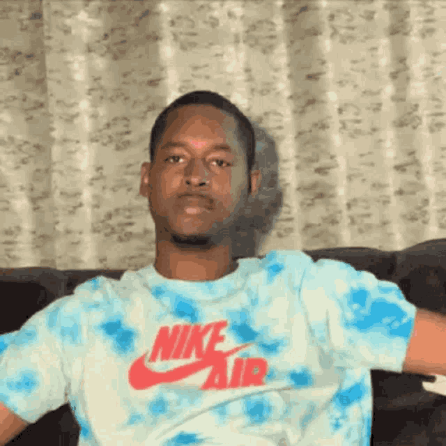 a man is sitting on a couch wearing a blue and white tie dye nike air shirt .