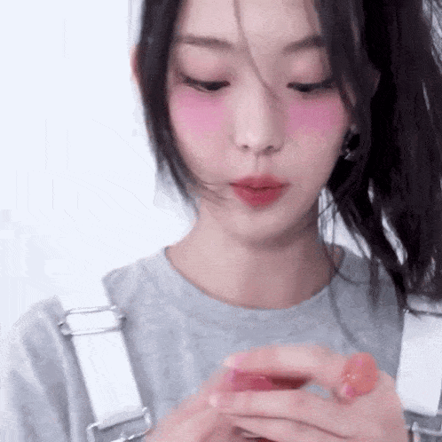 a close up of a woman wearing overalls and a gray shirt holding a pink object in her hands .