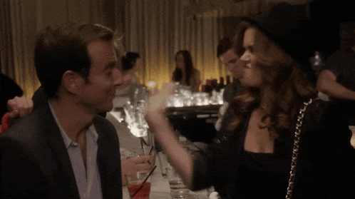 a woman in a black hat is pointing at a man with playing cards in front of his face