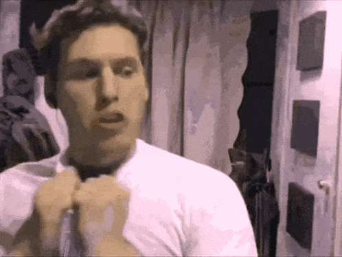 a man in a white shirt is adjusting his tie in a room