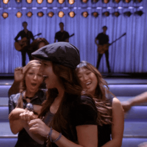 a woman wearing a hat is hugging another woman in front of a band