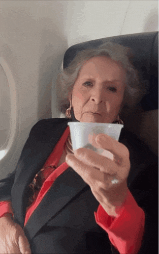 an elderly woman sitting on an airplane holding a cup of coffee