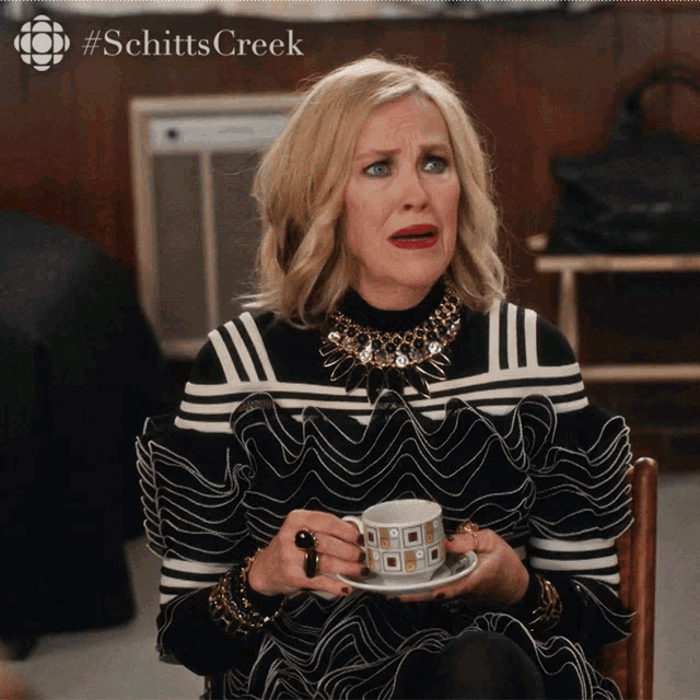 a woman is sitting in a chair holding a cup of coffee and a saucer with #schitts creek on the bottom