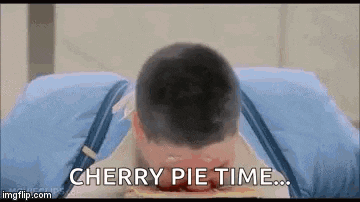 a man is laying on a bed with a cherry pie in his mouth and says `` cherry pie time '' .