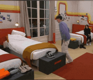 a man in a purple shirt is standing in a bedroom with two beds