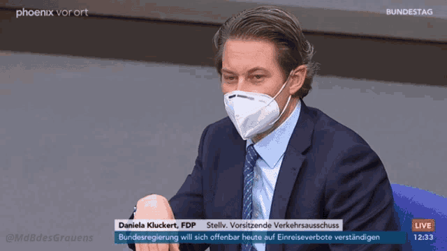 a man in a suit and tie wearing a face mask is on a live broadcast