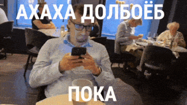 a man sitting at a table looking at his phone with a caption in russian that says " пока "