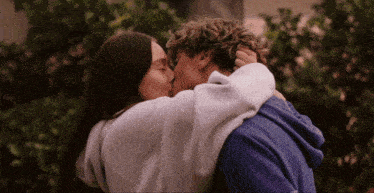 a man in a blue hoodie is kissing a woman in a white hoodie