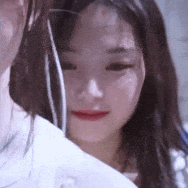 a close up of a woman 's face with her eyes closed and a white shirt on .