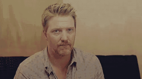 a man with a beard and blonde hair is sitting on a couch looking at the camera .