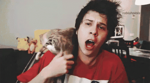a man in a red shirt is holding a cat with his mouth wide open