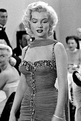 a black and white photo of a woman in a dress standing in front of a crowd of people .