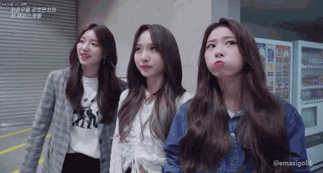 three girls are standing next to each other in front of a vending machine .