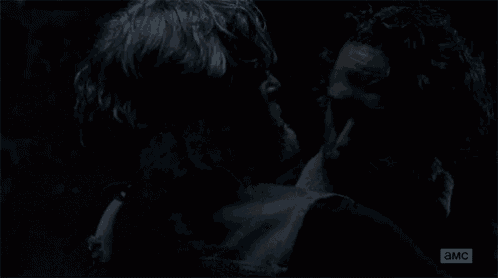 a man in a leather vest is standing next to another man in a dark room .