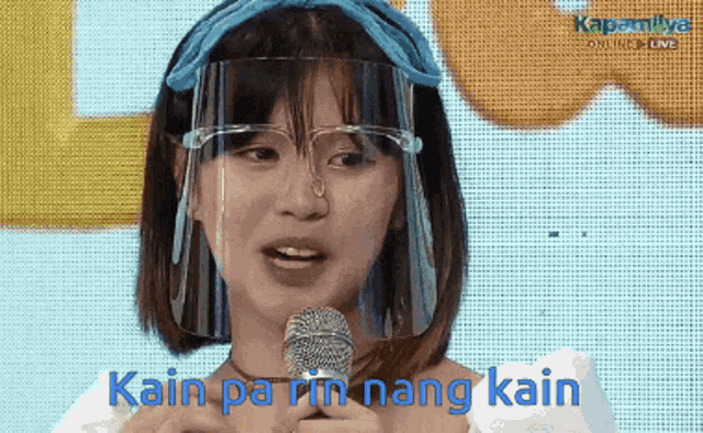 a woman wearing a face shield and glasses is speaking into a microphone