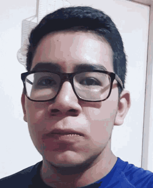 a young man wearing glasses and a blue shirt is making a funny face