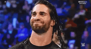 a man with long hair and a beard is smiling in front of a crowd on a wrestling show .