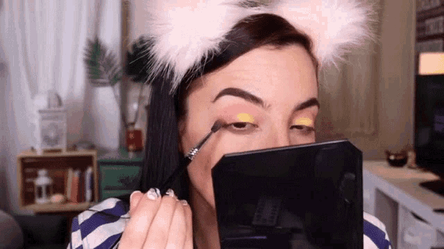 a woman wearing a furry headband is applying makeup in front of a mirror