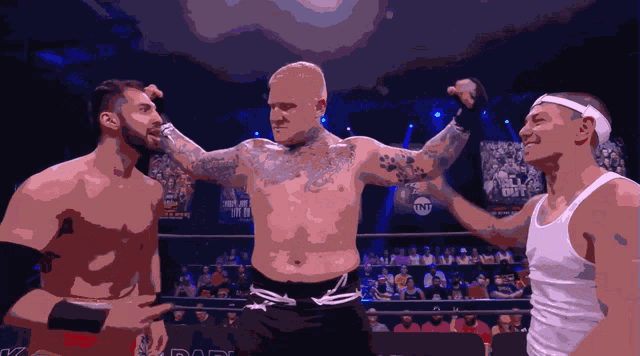 a man in a white tank top stands in a ring with two other men