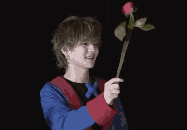 a young man is holding a red rose in his hand