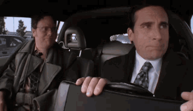 a man in a suit and tie is sitting in the back seat of a car with another man