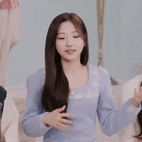 a girl in a blue sweater is smiling and making a heart shape with her hands