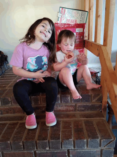 two little girls are sitting on a set of stairs and one of them is eating a slice of pizza