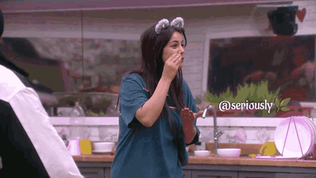 a woman covering her mouth with her hand in a kitchen with a sign that says @seriously on it