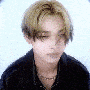 a young man with blonde hair and a black jacket is wearing a necklace .