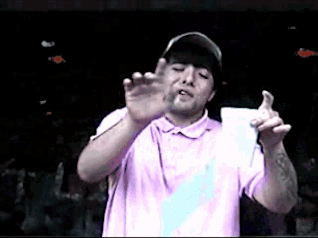 a man wearing a pink shirt and a hat is giving a thumbs up