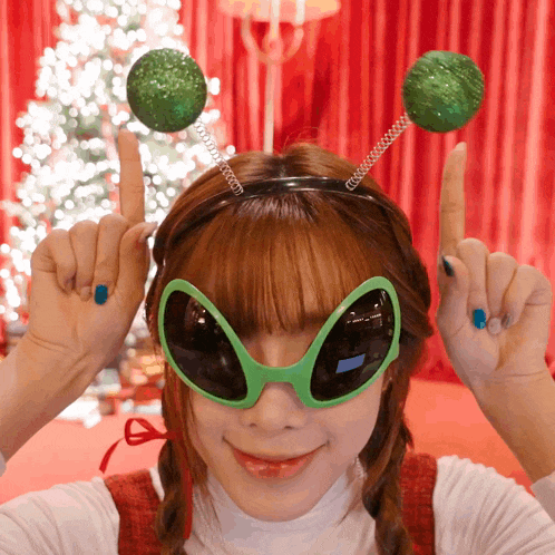 a woman wearing green alien sunglasses and a headband with green balls on it