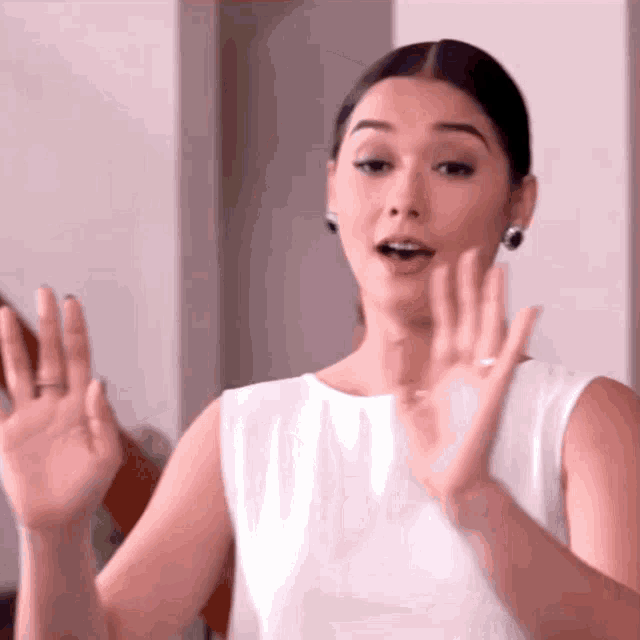 a woman in a white dress is making a gesture with her hands