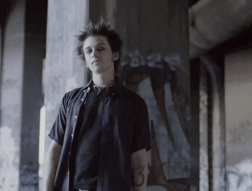 a young man in a black shirt stands in front of a wall with graffiti on it that says blaze