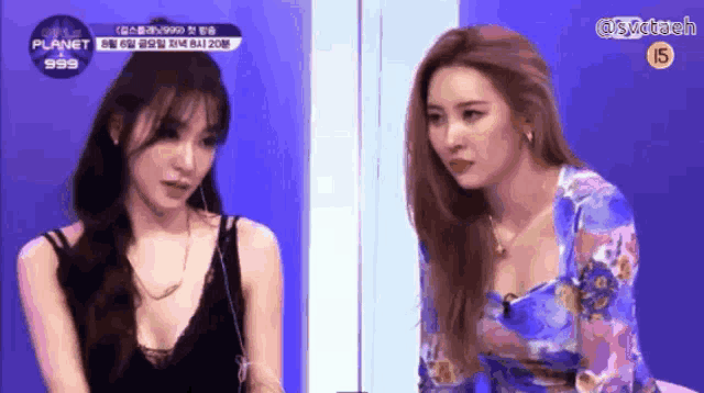 two women are sitting next to each other on a stage with the words planet 999 on the bottom