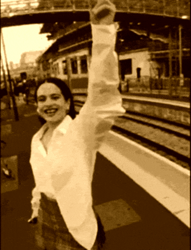 a woman in a white shirt is smiling and holding her arm up in the air