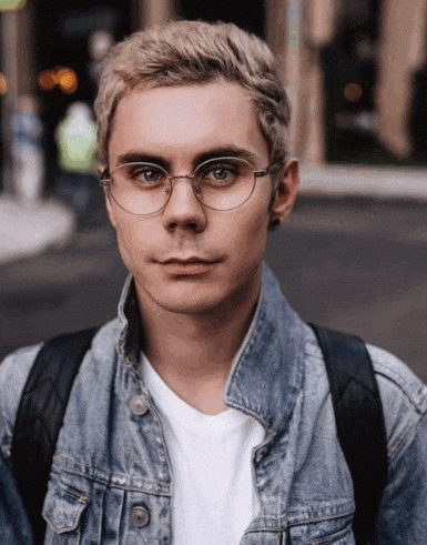 a young man wearing glasses and a denim jacket is looking at the camera