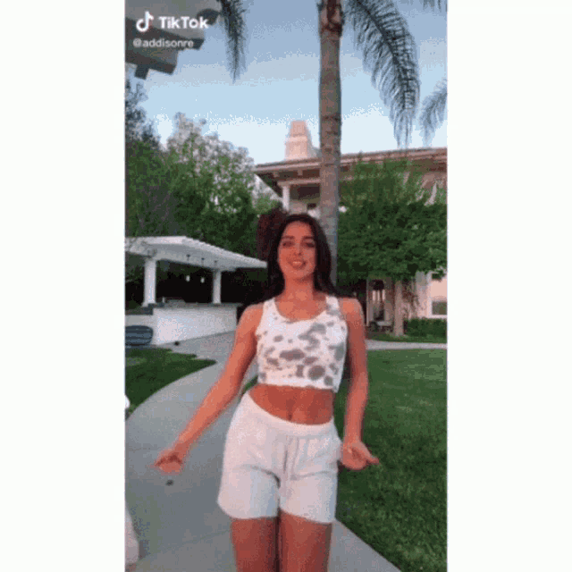 a woman in a crop top and white shorts is dancing on a sidewalk .