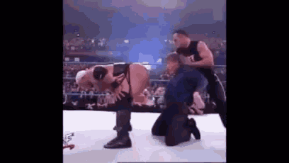 a wrestler is kneeling down on the ground while another wrestler holds his back .