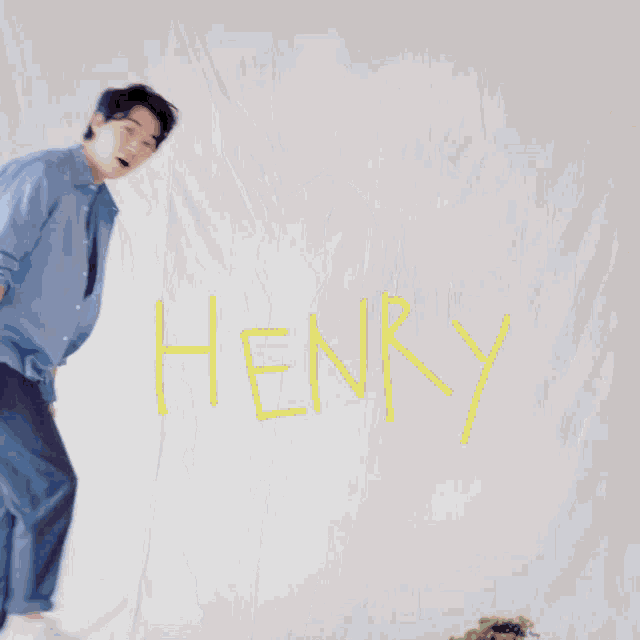a man in a blue shirt is dancing in front of a white cloth that says henry