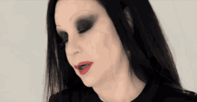 a woman with black hair and red lipstick looks down