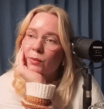 a woman with glasses is sitting in front of a microphone .