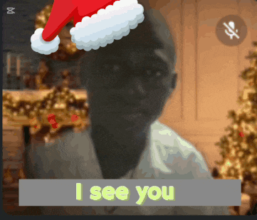 a man wearing a santa hat says i see you in front of a christmas tree