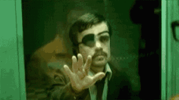 a man wearing sunglasses and a patch on his eye is standing in front of a window .