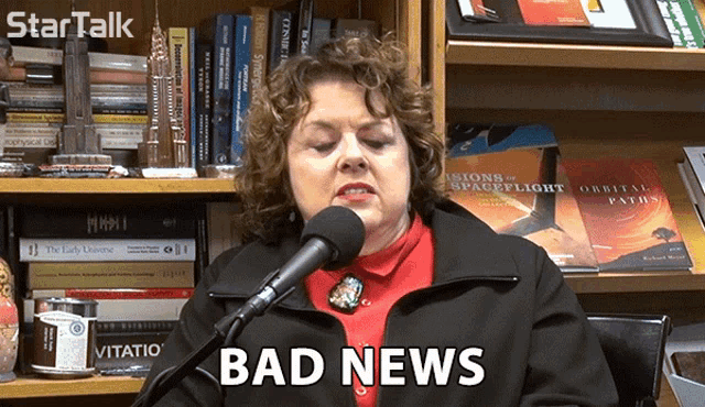 a woman is talking into a microphone and the words bad news are on the screen behind her