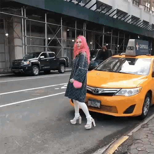 a woman with pink hair is standing in front of a yellow taxi that says capsule on the top