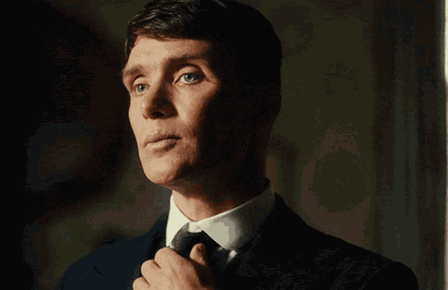 a man in a suit adjusts his tie in a dark room