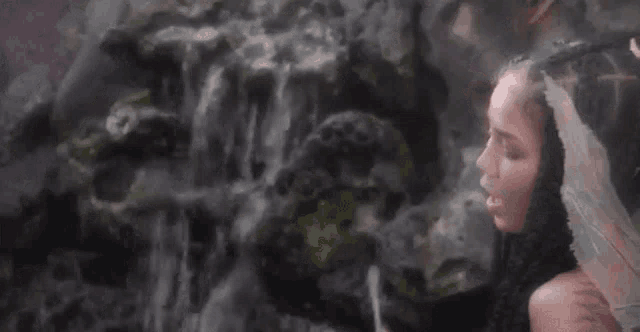 a woman is standing in front of a waterfall with her eyes closed and a veil on her head .